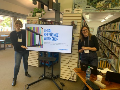 Rachel and Megan at Prince Rupert public library standing by a screen which says legal reference lab