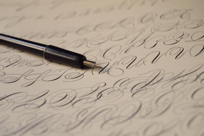 pen with a nib resting on a piece of paper covered with cursive writing