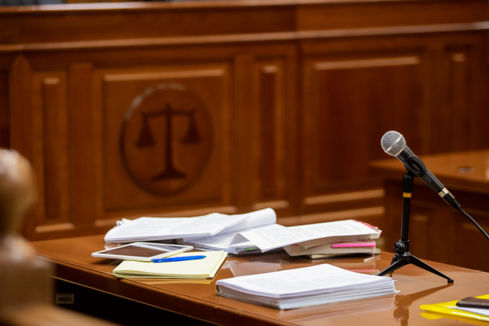 Close-up view from the perspective of the counsel table in a courtroom covered with documents and a microphone
