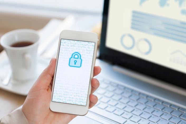 hand holding cell phone with lockey padlock on screen. laptop is open on the desk in the background