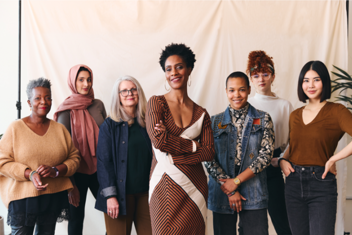 seven women of different ages, race, and shapes smiling into the camera