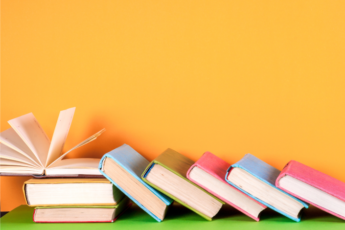 books laying slanted on a desk in front of a yellow background